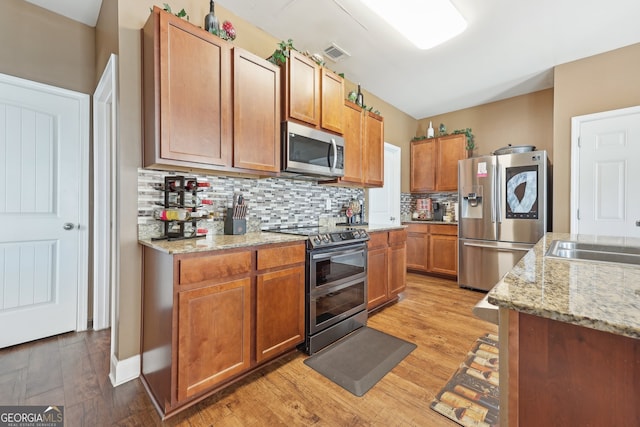 kitchen featuring light stone countertops, sink, light hardwood / wood-style flooring, backsplash, and appliances with stainless steel finishes