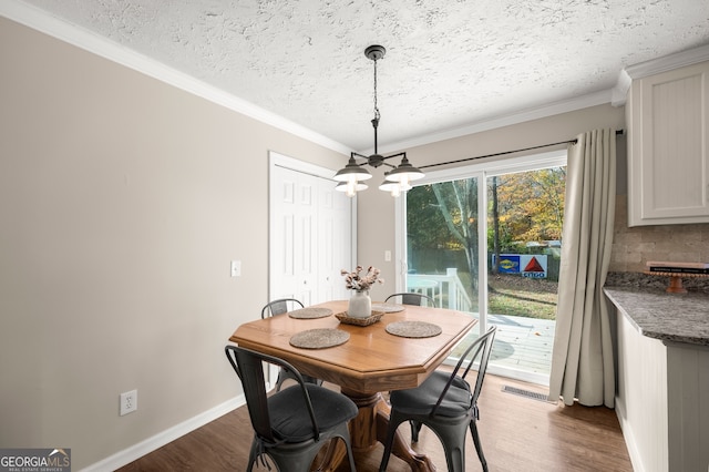 dining room with a notable chandelier, ornamental molding, a textured ceiling, and light wood-type flooring