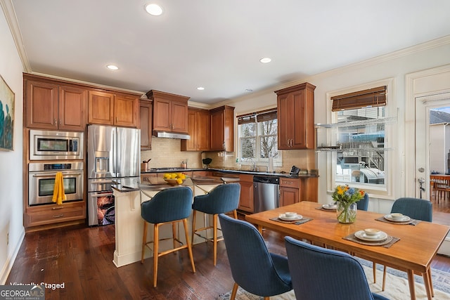 kitchen featuring dark wood-type flooring, ornamental molding, appliances with stainless steel finishes, and decorative backsplash