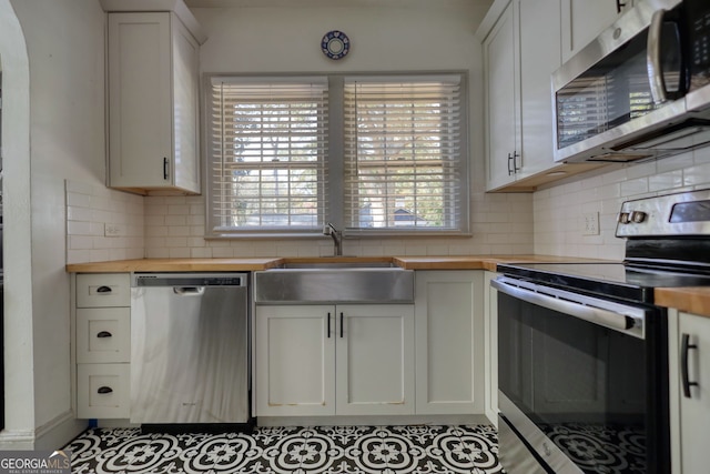 kitchen with wooden counters, white cabinets, sink, decorative backsplash, and appliances with stainless steel finishes