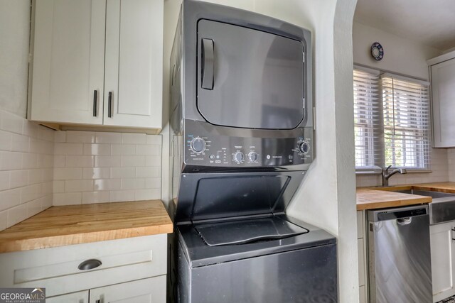 kitchen featuring dishwasher, stacked washing maching and dryer, tasteful backsplash, wooden counters, and white cabinets