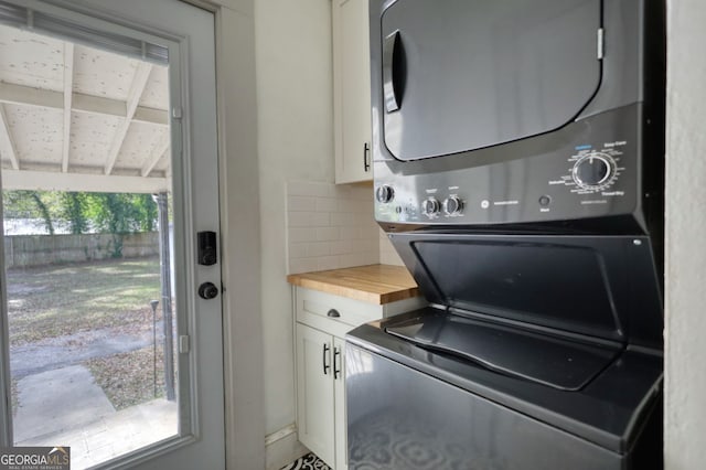 laundry area featuring stacked washer / drying machine and cabinets