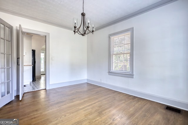 empty room featuring a textured ceiling, hardwood / wood-style flooring, ornamental molding, and a notable chandelier