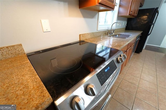 kitchen featuring light stone counters, black fridge, sink, stainless steel range with electric cooktop, and light tile patterned flooring