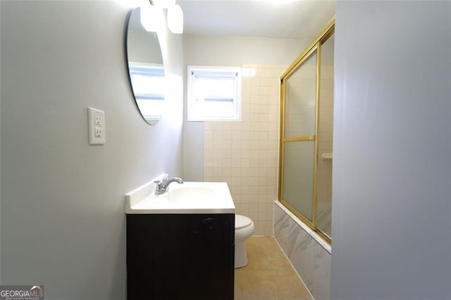 full bathroom featuring tile patterned floors, bath / shower combo with glass door, toilet, vanity, and tile walls