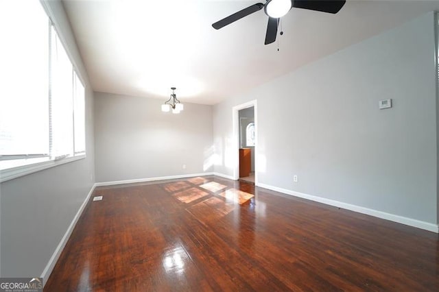 spare room with ceiling fan with notable chandelier and dark wood-type flooring