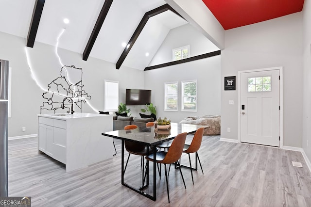 dining area featuring beamed ceiling, a healthy amount of sunlight, light wood-type flooring, and high vaulted ceiling