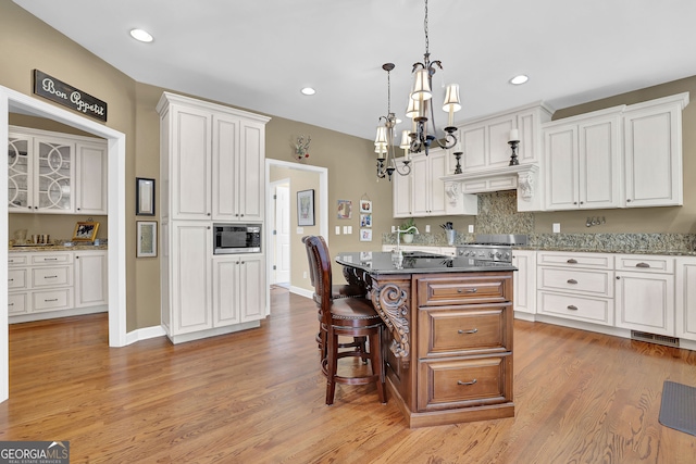 kitchen featuring a kitchen island, dark stone countertops, decorative light fixtures, light hardwood / wood-style floors, and white cabinetry