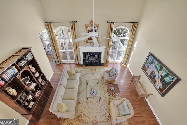 living room with a towering ceiling, hardwood / wood-style flooring, a healthy amount of sunlight, and a premium fireplace