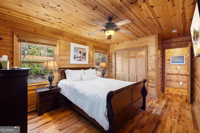 bedroom featuring ceiling fan, light hardwood / wood-style floors, wooden walls, a closet, and wood ceiling