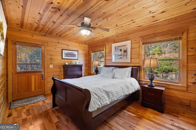 bedroom with ceiling fan, light hardwood / wood-style flooring, wood ceiling, and wooden walls