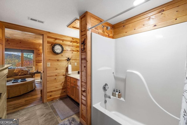 bathroom with wooden walls, shower / washtub combination, vanity, and a textured ceiling