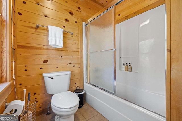 bathroom with combined bath / shower with glass door, tile patterned floors, wooden walls, and toilet