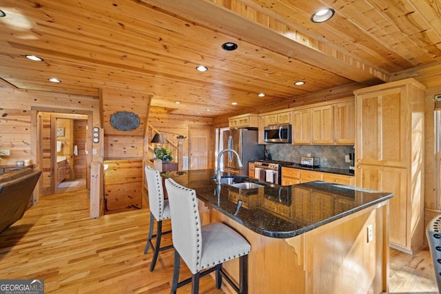 kitchen with appliances with stainless steel finishes, light wood-type flooring, a large island, and wood walls