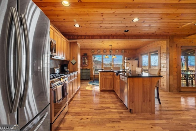 kitchen with stainless steel appliances, a kitchen island with sink, decorative light fixtures, wooden ceiling, and light hardwood / wood-style floors