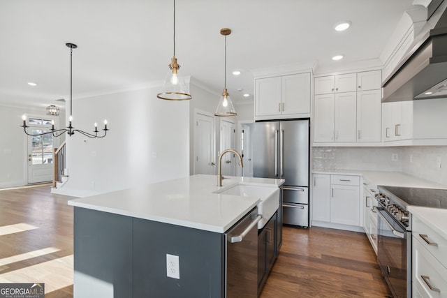 kitchen featuring high quality appliances, white cabinetry, hanging light fixtures, a center island with sink, and wall chimney range hood