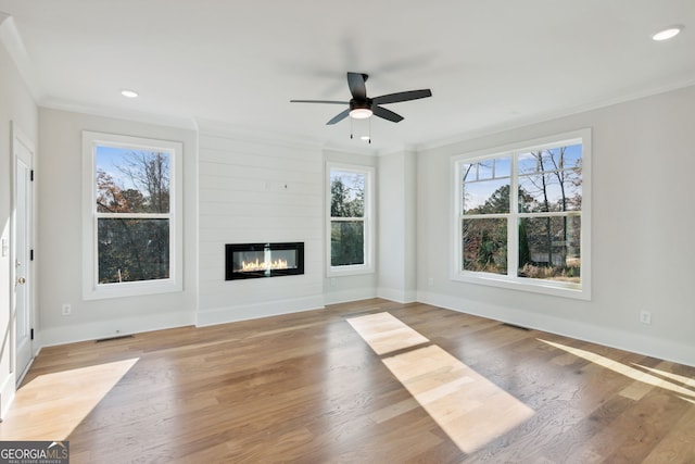 unfurnished living room with hardwood / wood-style flooring, ornamental molding, a large fireplace, and ceiling fan