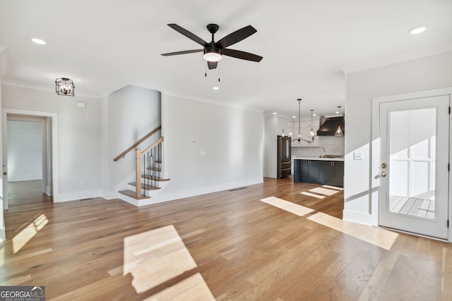 unfurnished living room with crown molding, ceiling fan with notable chandelier, and light wood-type flooring