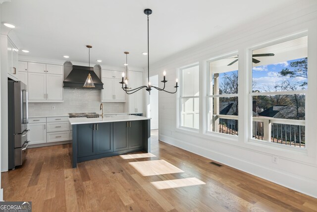 kitchen with premium range hood, pendant lighting, an island with sink, high end refrigerator, and white cabinets