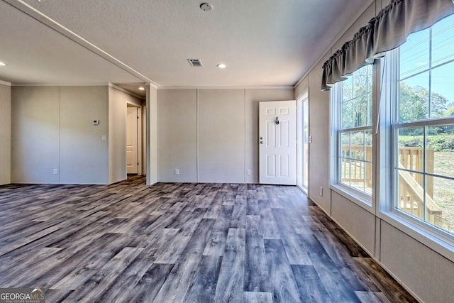 empty room featuring crown molding, dark wood-type flooring, and a wealth of natural light