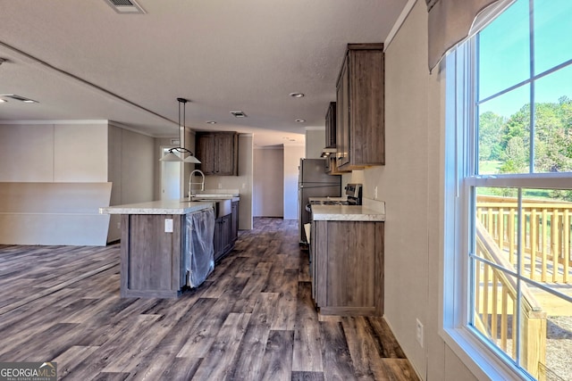 kitchen featuring dark hardwood / wood-style flooring, crown molding, sink, hanging light fixtures, and an island with sink