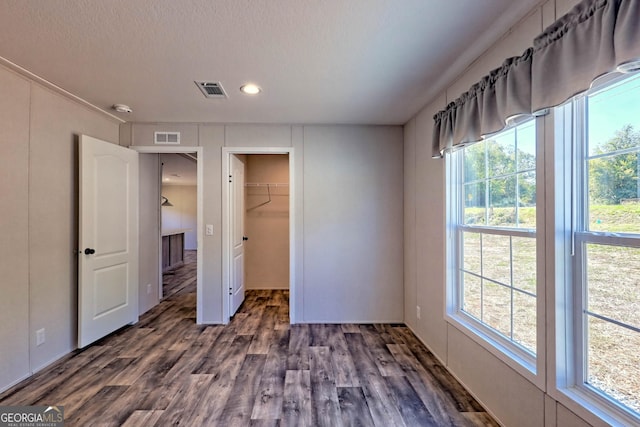 unfurnished bedroom featuring a walk in closet, dark hardwood / wood-style flooring, a closet, and a textured ceiling