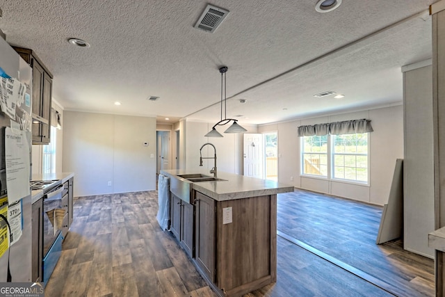 kitchen with pendant lighting, sink, stainless steel electric range, dark wood-type flooring, and a kitchen island with sink