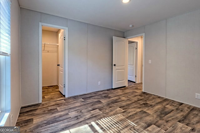 unfurnished bedroom featuring a walk in closet, a closet, and dark hardwood / wood-style floors