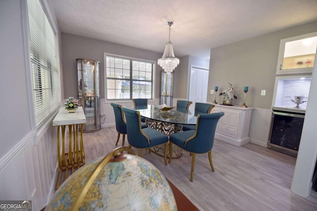 dining room with wine cooler, a chandelier, a textured ceiling, and light wood-type flooring