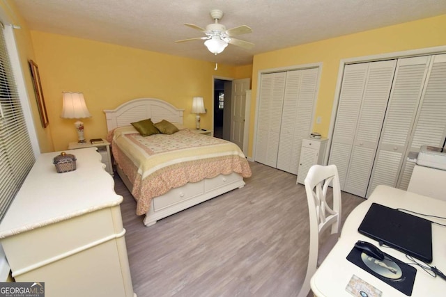 bedroom featuring hardwood / wood-style flooring, ceiling fan, a textured ceiling, and two closets