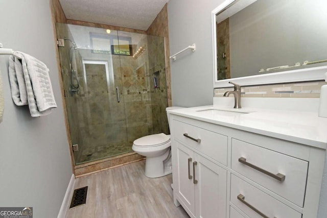 bathroom with tasteful backsplash, vanity, a shower with door, hardwood / wood-style floors, and toilet