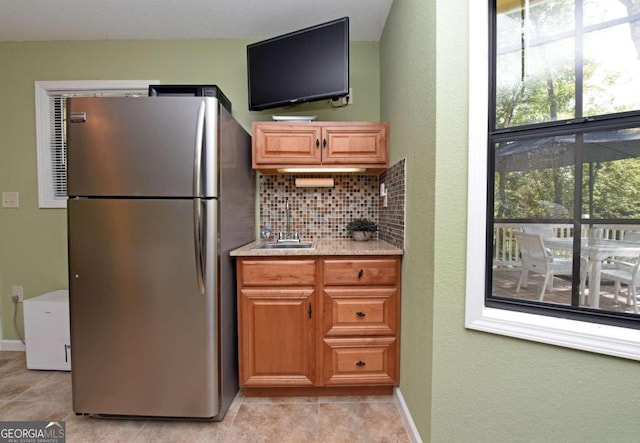 kitchen featuring light tile patterned floors, tasteful backsplash, stainless steel refrigerator, and sink