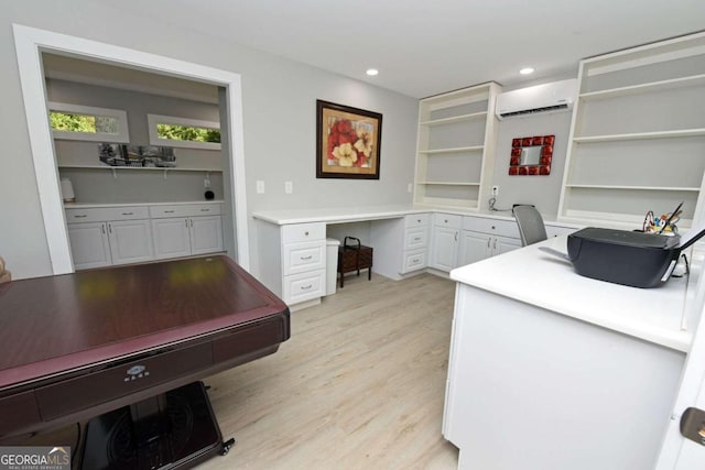 home office featuring light wood-type flooring, an AC wall unit, and built in desk