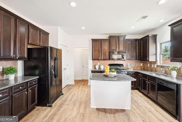 kitchen featuring black appliances, light hardwood / wood-style floors, dark stone countertops, and sink