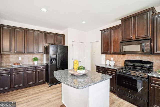 kitchen featuring decorative backsplash, light wood-type flooring, a center island, and black appliances