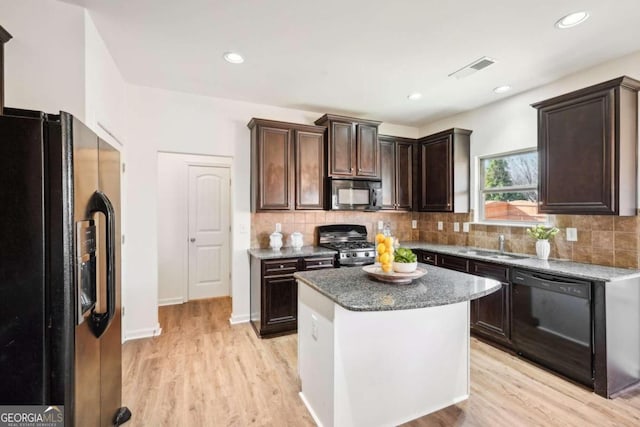 kitchen with backsplash, black appliances, sink, a kitchen island, and light hardwood / wood-style floors