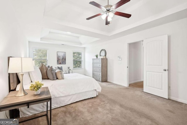 carpeted bedroom with a raised ceiling and ceiling fan