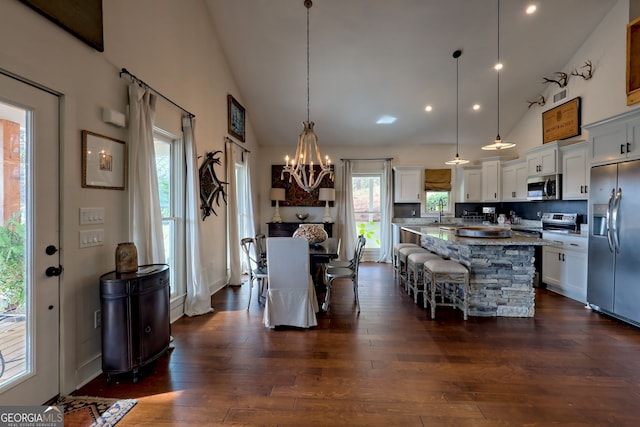 kitchen featuring white cabinets, appliances with stainless steel finishes, hanging light fixtures, light stone counters, and a breakfast bar