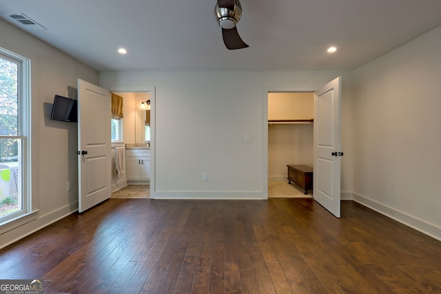 unfurnished bedroom featuring ensuite bathroom, a walk in closet, ceiling fan, and dark wood-type flooring