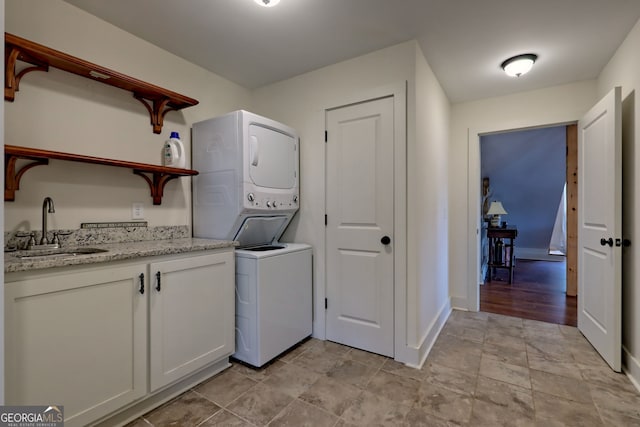 clothes washing area featuring cabinets, sink, and stacked washer / dryer