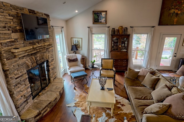 living room with lofted ceiling, plenty of natural light, a stone fireplace, and hardwood / wood-style floors