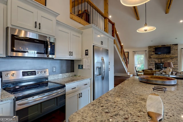 kitchen featuring a fireplace, pendant lighting, white cabinetry, light stone countertops, and appliances with stainless steel finishes