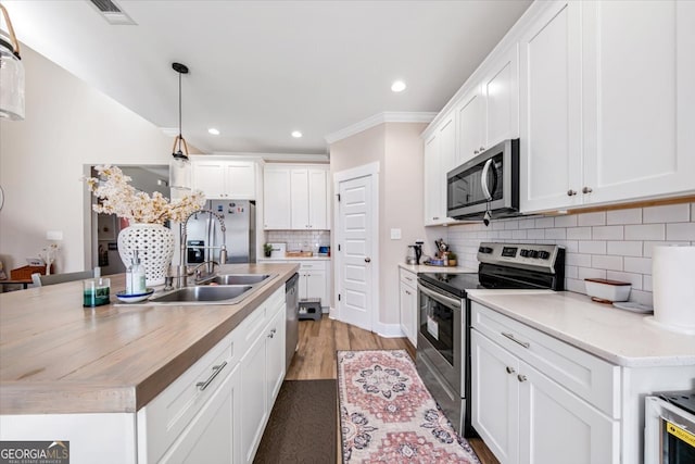 kitchen with white cabinets, decorative light fixtures, light wood-type flooring, and stainless steel appliances