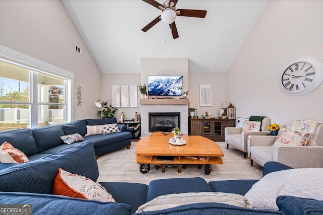 living room with ceiling fan, light wood-type flooring, a tile fireplace, and high vaulted ceiling