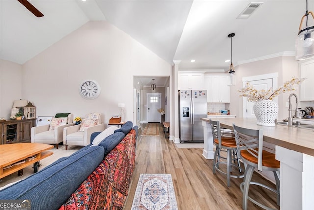 living room with ceiling fan, sink, light hardwood / wood-style flooring, high vaulted ceiling, and ornamental molding