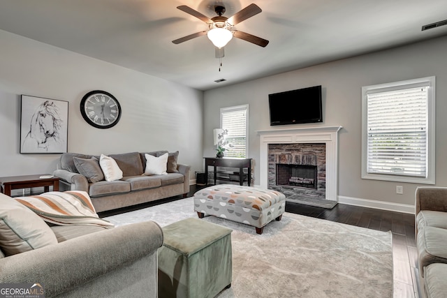 living room with dark hardwood / wood-style floors, a stone fireplace, ceiling fan, and a healthy amount of sunlight