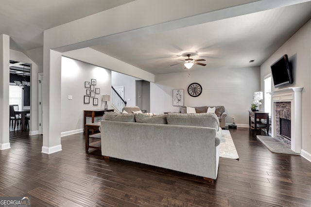 living room with ceiling fan, a stone fireplace, and dark wood-type flooring