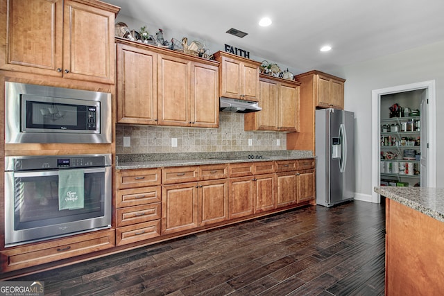 kitchen with light stone countertops, appliances with stainless steel finishes, backsplash, and dark wood-type flooring