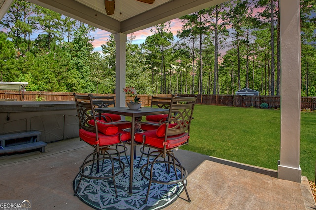 patio terrace at dusk featuring ceiling fan and a yard