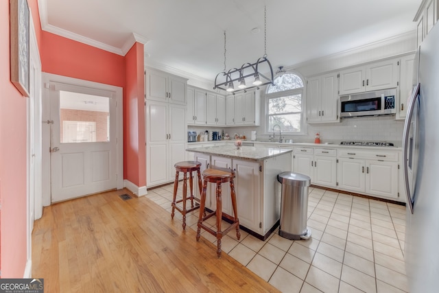 kitchen with white cabinets, decorative light fixtures, a kitchen island, and appliances with stainless steel finishes